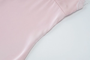 Close-up of pink satin fabric with delicate white lace trim and glossy silk texture