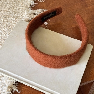 Dettaglio ravvicinato di un cerchietto largo in peluche caramello con texture morbida ed etichetta