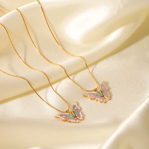 Close-up of dual gold butterfly pendants with gradient enamel inlay on silk fabric