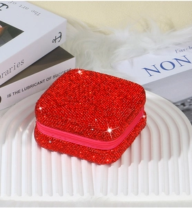 Close-up of a square red rhinestone jewelry box with a zipper closure on a white tray