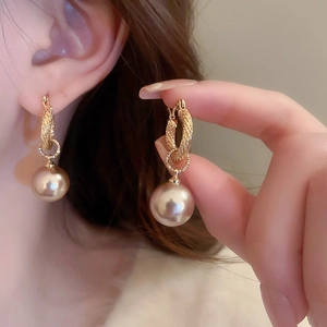 Detalle de pendientes de aro dorados texturizados con un gran colgante de perla real