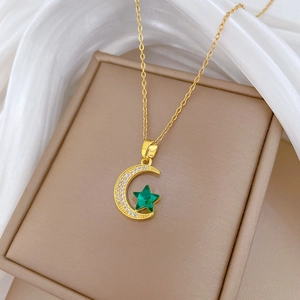 Macro detail of gold moon necklace with green star gemstone on silk background