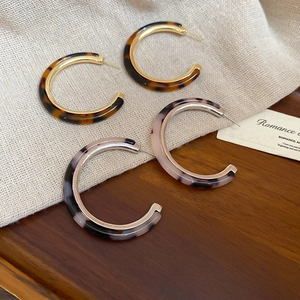Close-up of resin C-shape earrings with amber and marble patterns on wooden display