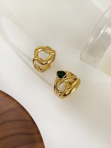 Detailed shot of gold plated chain ring and green heart gemstone ring on white stand