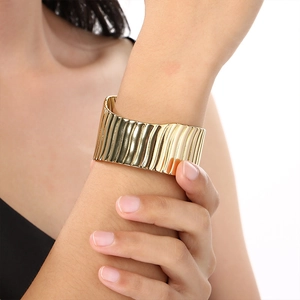 Macro shot of gold wide cuff bracelet with wavy texture and metallic pleated surface detail