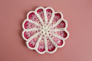 Top-down view of a handmade crochet flower coaster with pink gradient petals and white edge