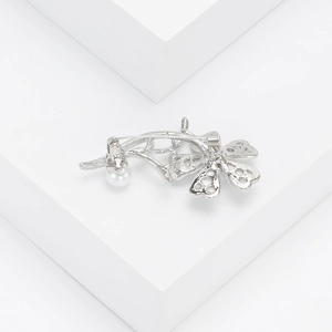 Detailed view of silver flower brooch featuring a white pearl on a minimalist background