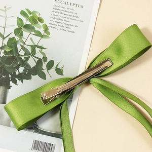 Green ribbon bow hair clip with metal duckbill clasp displayed on a stylish magazine