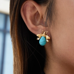 Detailed view of a gold bee earring with turquoise body worn on a female ear