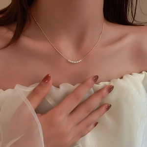 Close-up of a delicate gold chain necklace with a curved pearl pendant on a model's neck