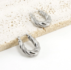 Detail view of silver twisted U-shape hoop earrings on a textured stone surface