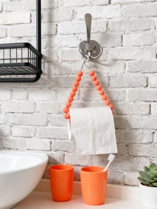 Detail of vibrant orange beaded toilet paper holder on white stone bathroom wall
