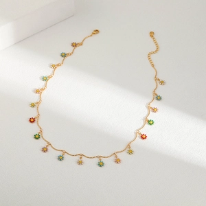 Detail view of gold chain necklace featuring colorful enamel daisy pendants on white background