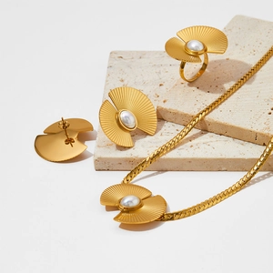 Vintage-Schmuckset aus goldenem Edelstahl mit Fächerperlen auf beigen Steinplatten