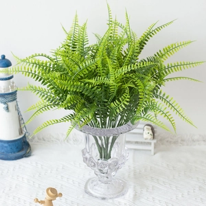 Lush artificial Boston fern in textured clear glass vase on a white tabletop setting