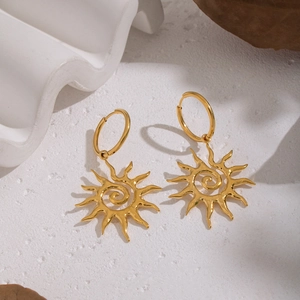 Golden sun earrings with spiral design on textured white surface with dry leaves