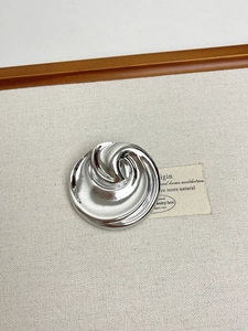 Macro detail of silver whirlpool metal brooch on linen background for suits
