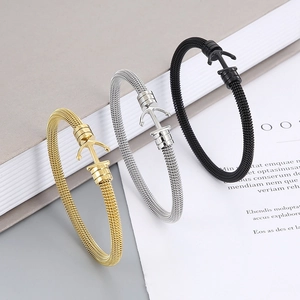 Three steel cable anchor bracelets in gold, silver, and black finishes on a book