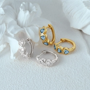 Detailed view of gold and silver huggie earrings with heart-shaped gemstone accents