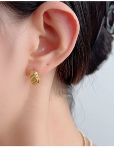Close-up of a gold croissant twisted earring worn on the earlobe with minimalist style