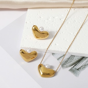 Close-up of gold heart necklace and pearl stud earrings set on silk background