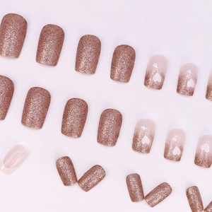 Rose gold glitter press-on nails with white heart designs and gradient nude finish
