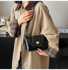 Detail of glossy black patent leather shoulder bag with golden metallic twist lock