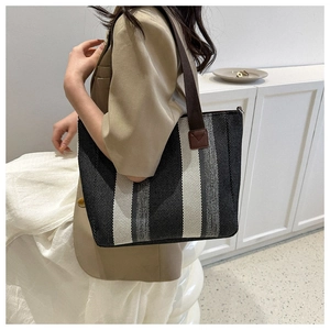 Close-up of a striped canvas tote bag with brown leather straps worn by a model