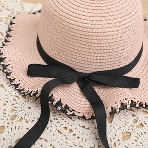 Detailed macro view of pink straw hat featuring black bow ribbon and wavy crochet edge