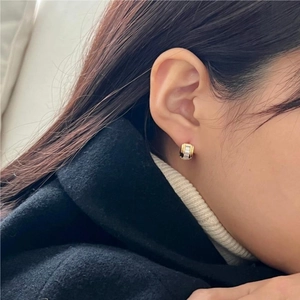 Close-up of minimalist gold huggie earrings with white inlay worn by a model