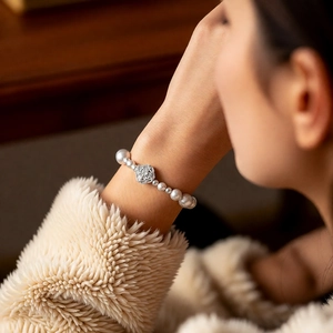Detail shot of pearl bracelet with rose flower pendant on a model wearing a soft knit