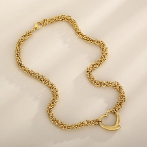 Top view of a gold braided chain necklace with a heart pendant on a soft beige background