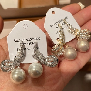 Macro shot of S925 silver bow earrings with large white pearls and micro-pave diamonds