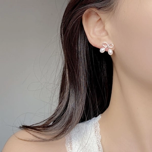 Détail des boucles d'oreilles nœud et perles portées montrant un style élégant
