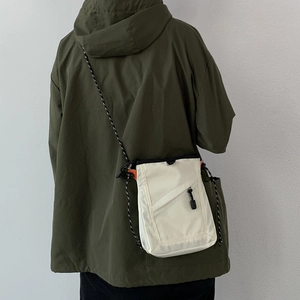 Detail of off-white canvas crossbody bag with woven rope strap worn over an olive parka