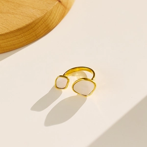 Detail of a gold open ring featuring square and round white stone inlays on a beige background