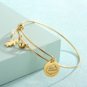 Détail d'un bracelet doré avec perle, breloque fille et gravure Merry Christmas