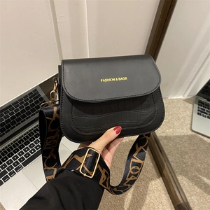 Chic black crocodile embossed crossbody bag with wide patterned strap and gold lettering