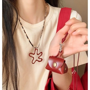Detail of red leather mini bag pendant with star charm and floral necklace on a model
