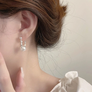 Elegant U-shaped silver earring detail featuring a large white pearl on a fashion model
