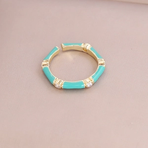 Bamboo style gold ring with teal enamel and cubic zirconia on soft pink velvet surface