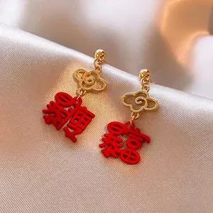 Detailed close-up of gold ear studs featuring red Chinese lucky charms on silk