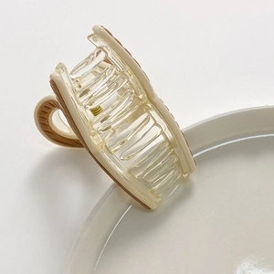 Close-up of a mini striped hair claw clip with brown pattern on a white ceramic plate