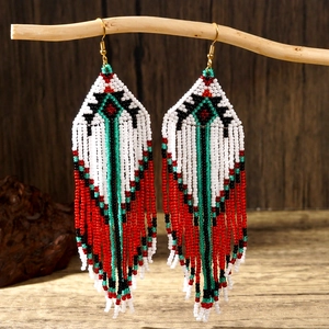 Handmade bohemian seed bead tassel earrings with geometric patterns on a wooden branch