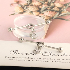 Detail of silver industrial barbell earrings with zircon star and moon pendants