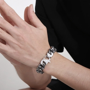 Macro detail of men's Cuban chain bracelet featuring skull carvings and spring clasp