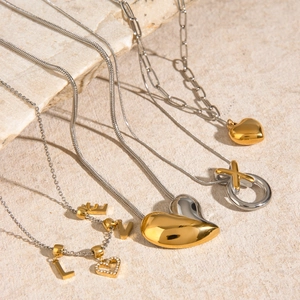 Gold and silver layered heart and letter pendant necklaces on a beige textured stone