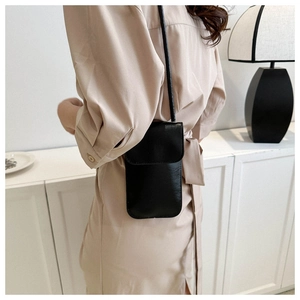 Minimalist black leather small crossbody phone bag shown on a model in a modern interior