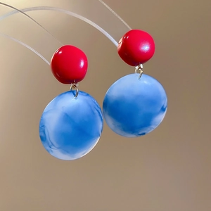 Detail of red and blue marble resin earrings hanging on a clear jewelry display stand