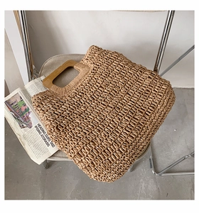 Detail of the woven straw handbag featuring a trapezoidal light wood handle and texture